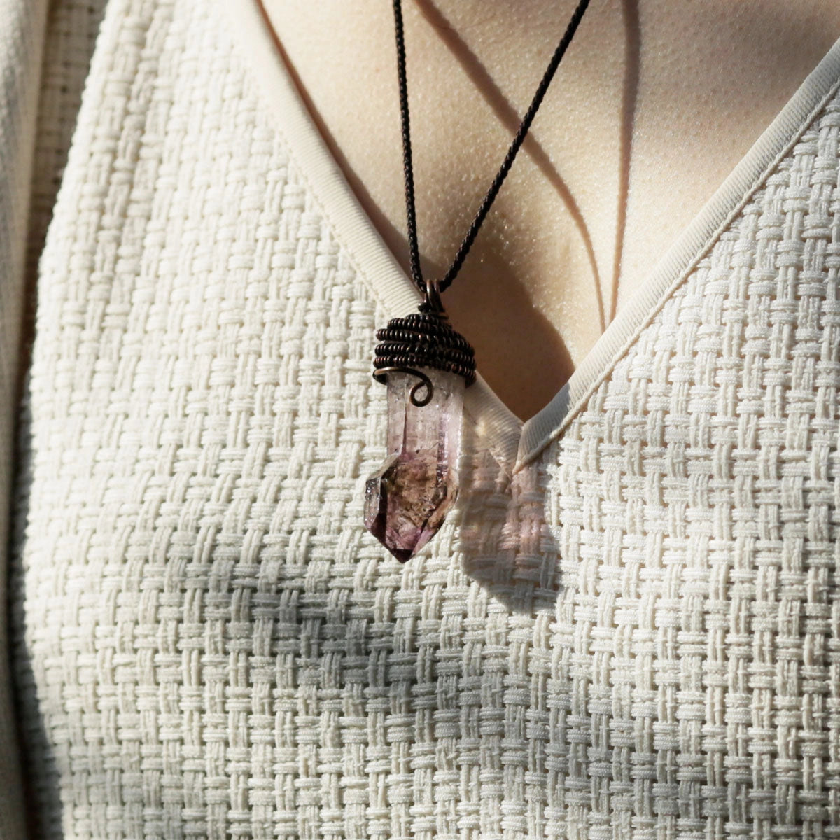 Two small crystal pendants on cords worn over a light knit top.