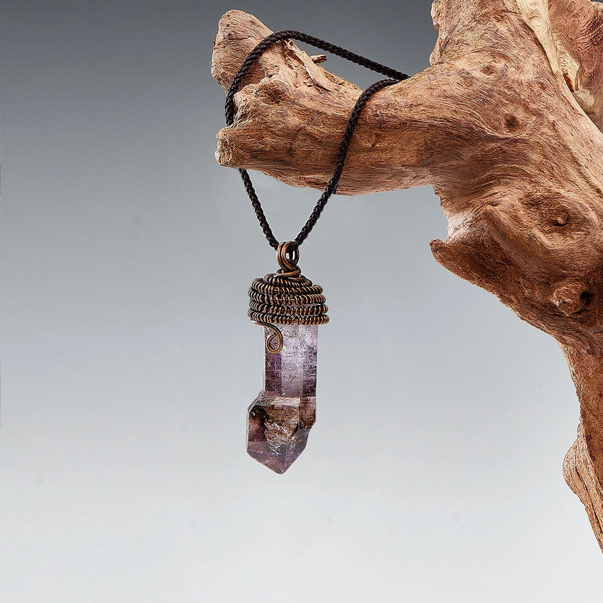 Pendant hanging from a wood branch with a soft gray backdrop.