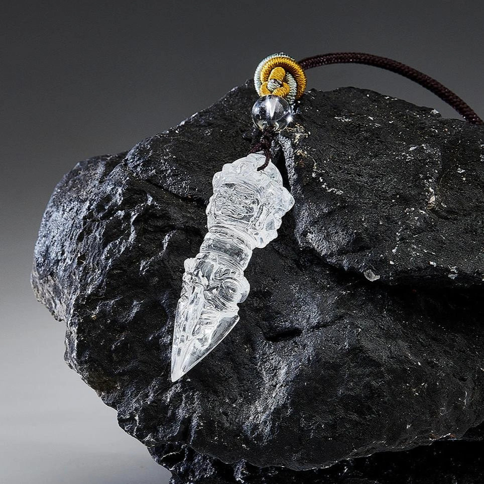 Clear carved crystal pendant with cord resting on a large black rock in studio light.