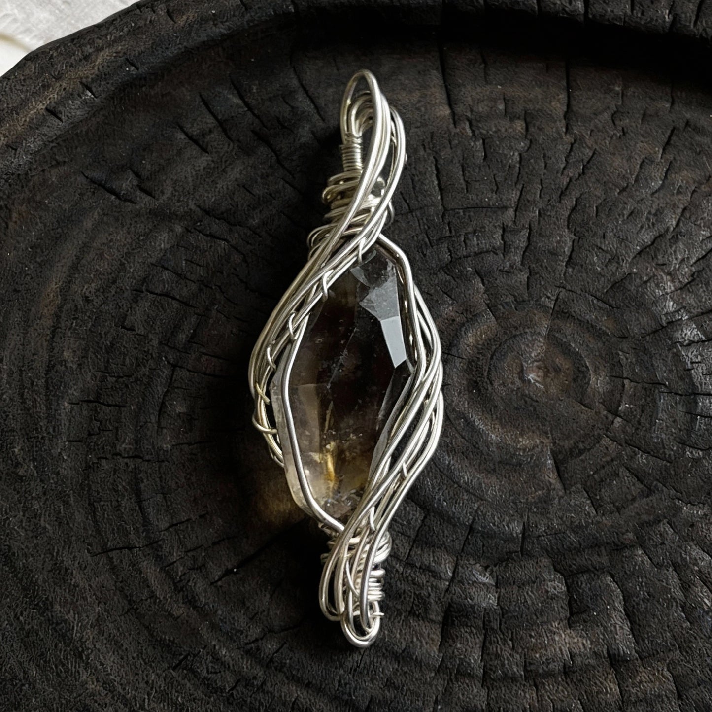Pendant standing upright on a dark wooden plate, front view.