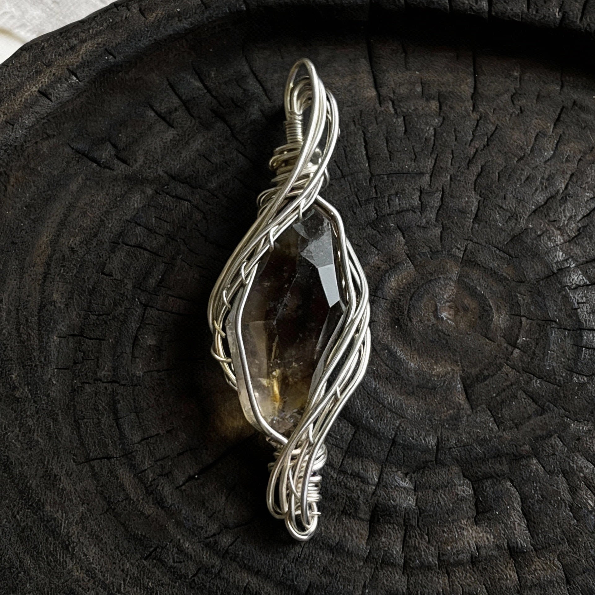 Pendant standing upright on a dark wooden plate, front view.