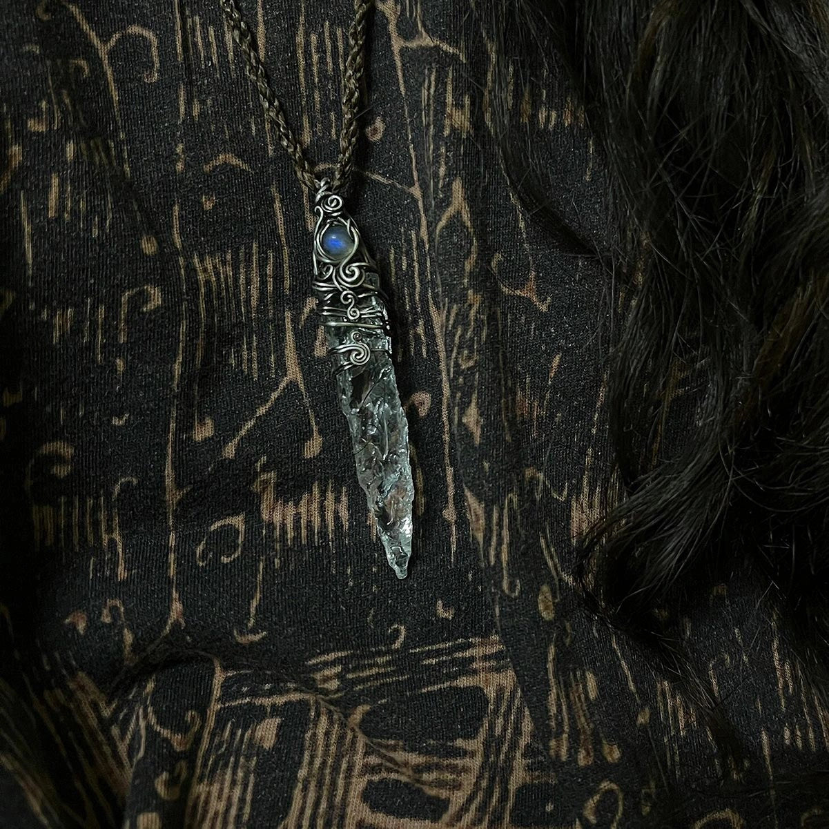 Pendant hanging against a dark patterned fabric background.