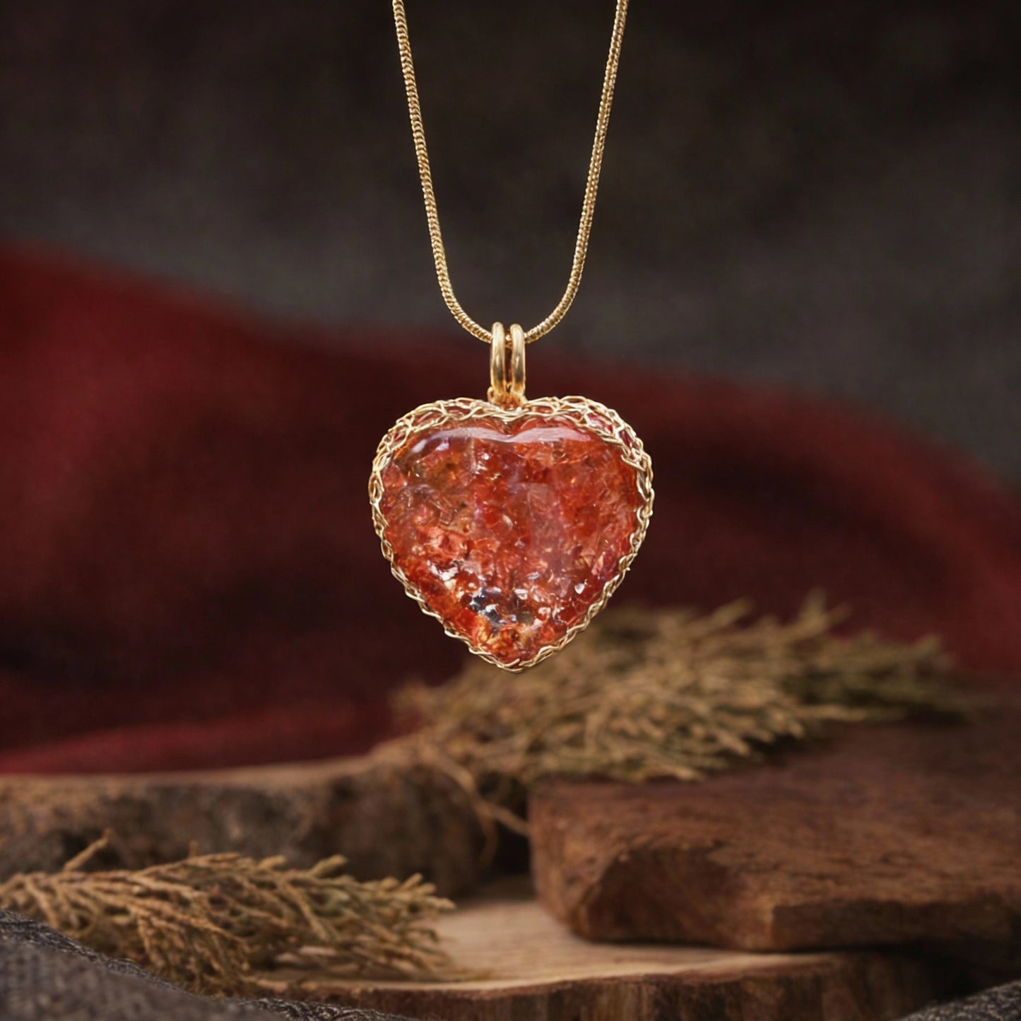 Pendant on a gold chain placed beside dried herbs on a wooden block.