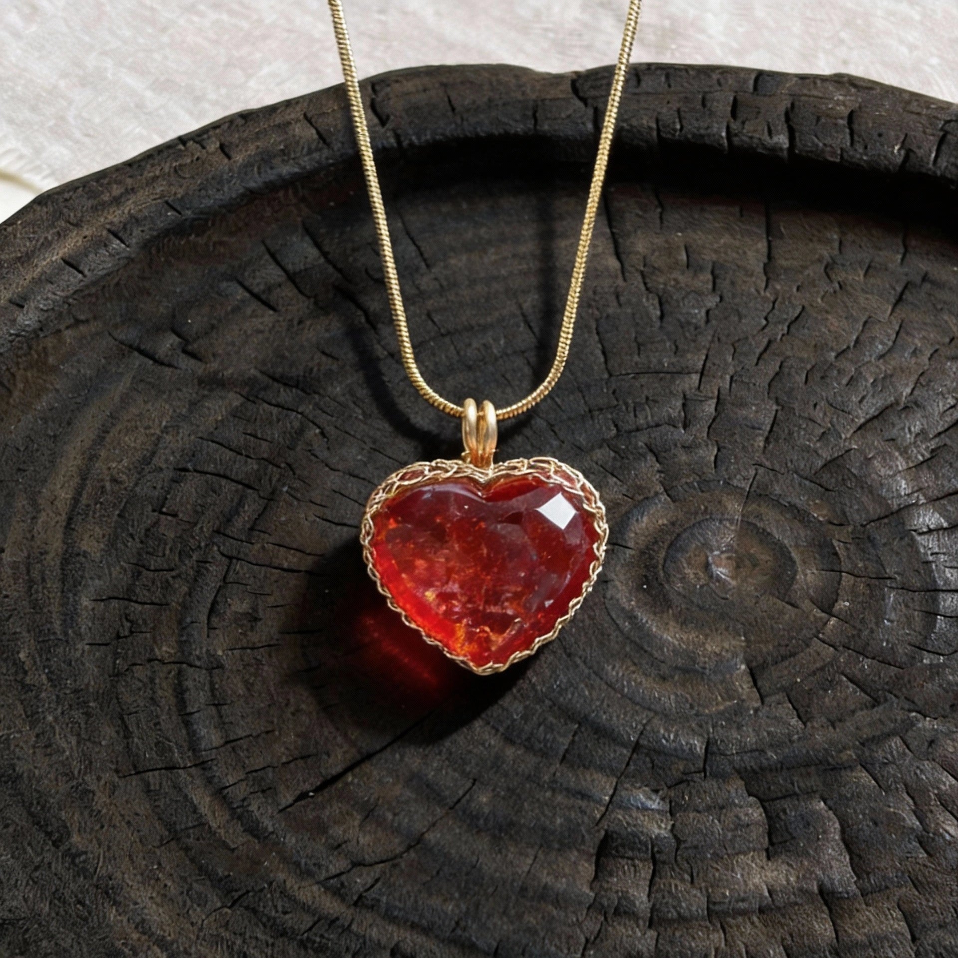 Red heart-shaped crystal pendant on a gold chain displayed on a dark wooden plate.