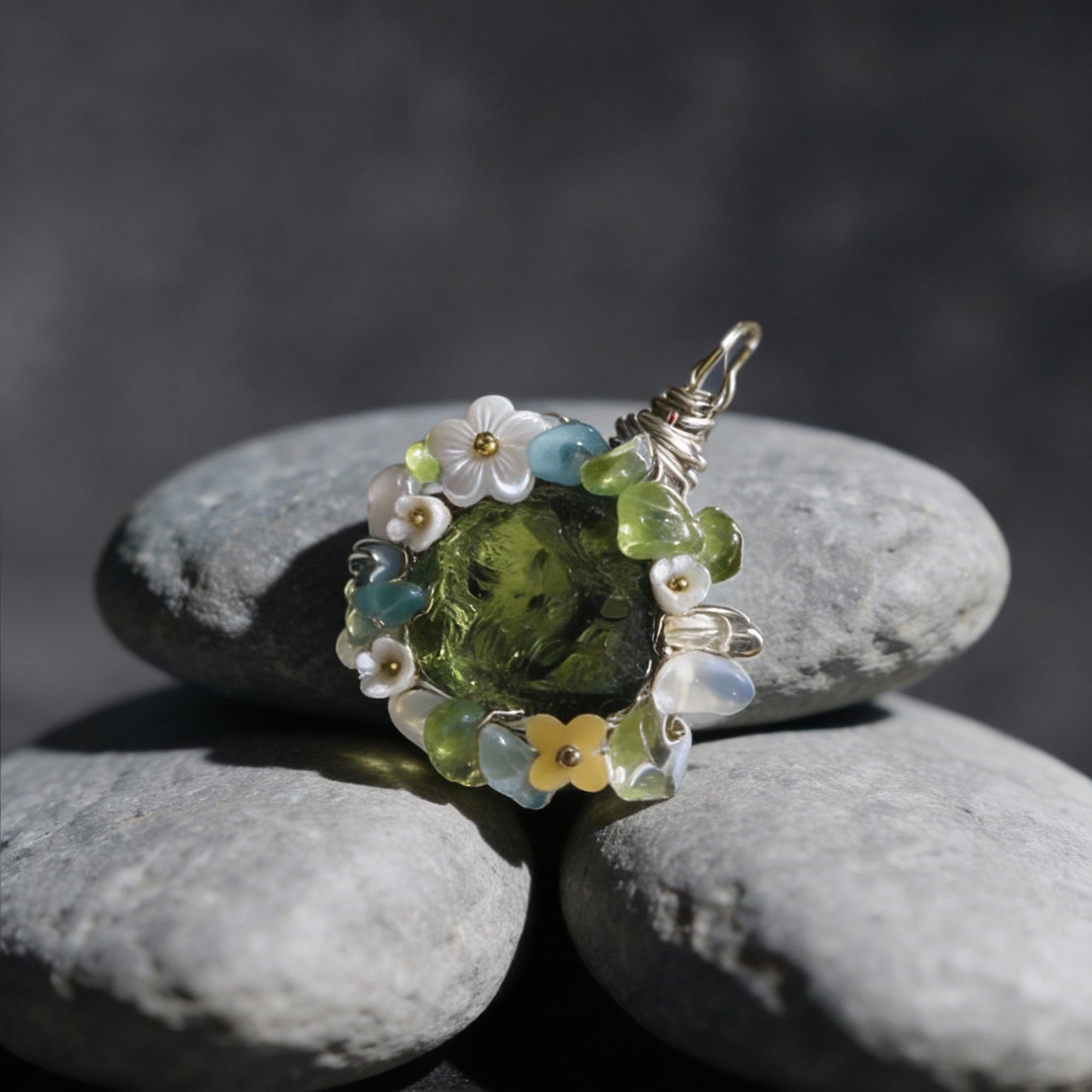 Pendant placed on stacked smooth gray river stones, dark background.