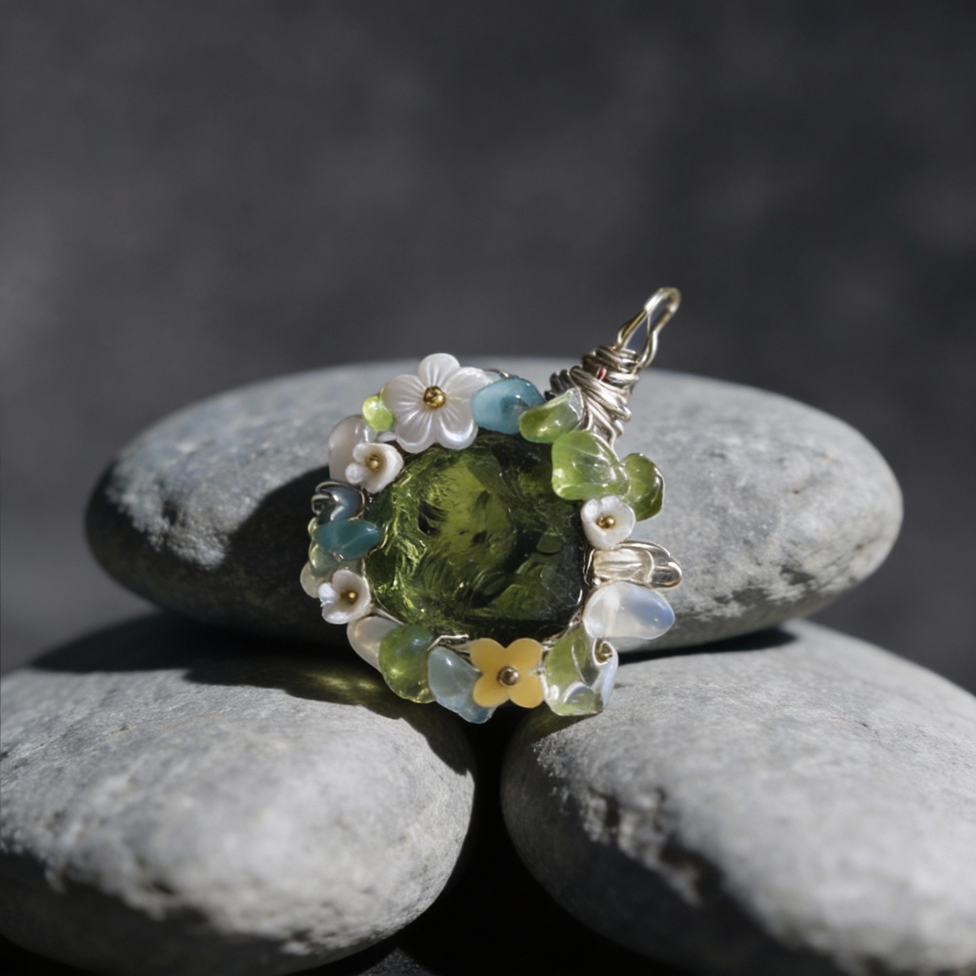 Pendant placed on stacked smooth gray river stones, dark background.