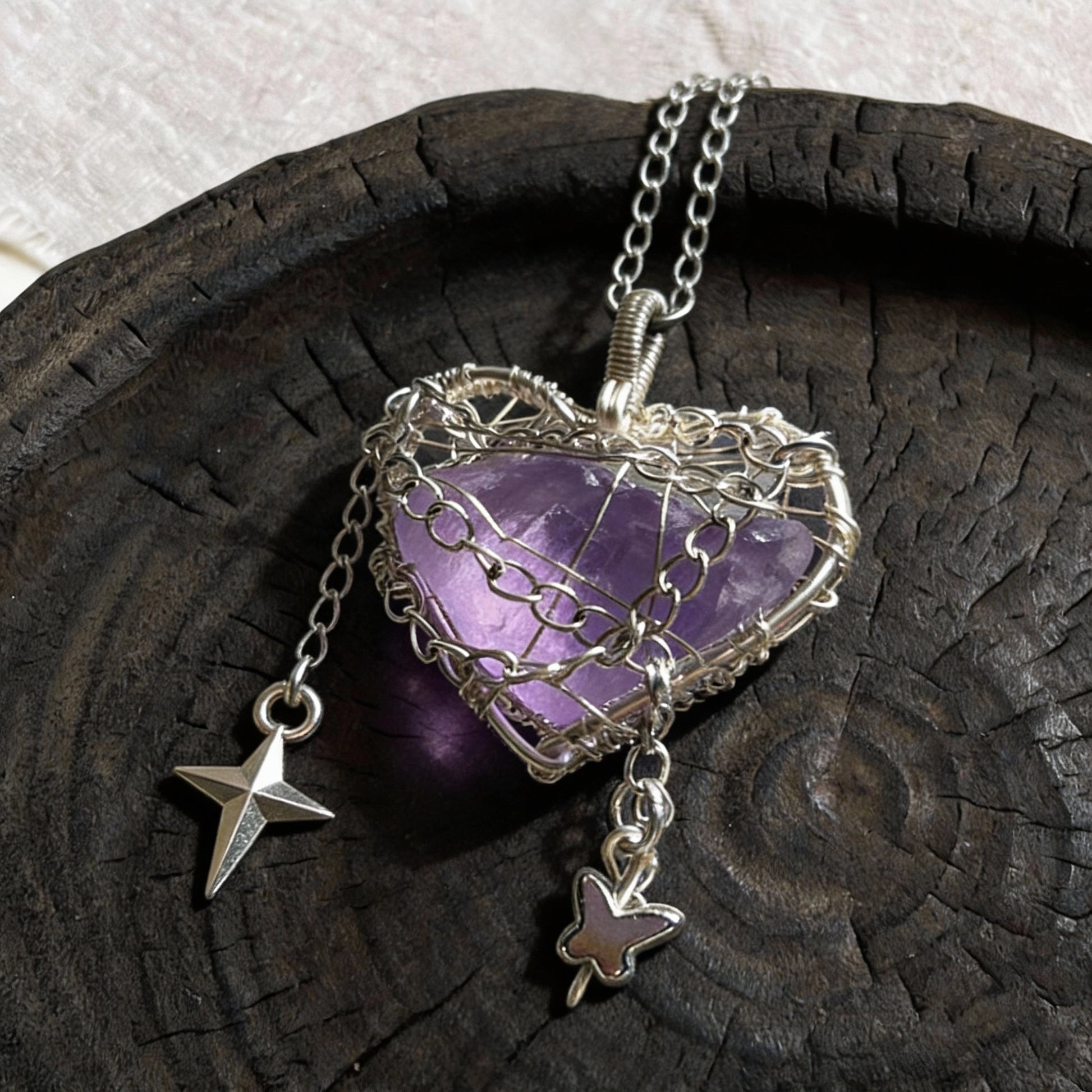 Pendant laid on a dark wooden plate with chain and dangling charms.