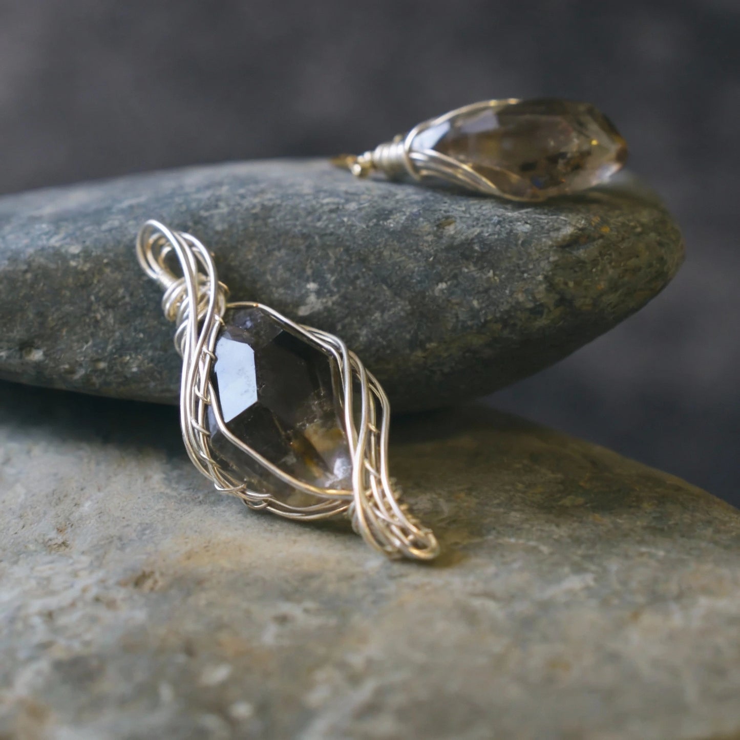 Pendant resting on stacked smooth gray stones, side angle.