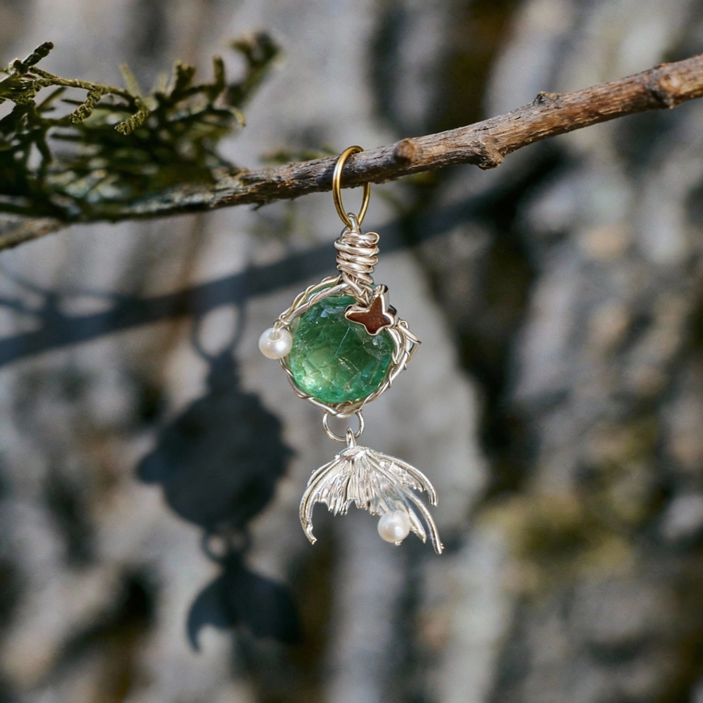 Pendant hanging from a small branch against a blurred tree-bark background.