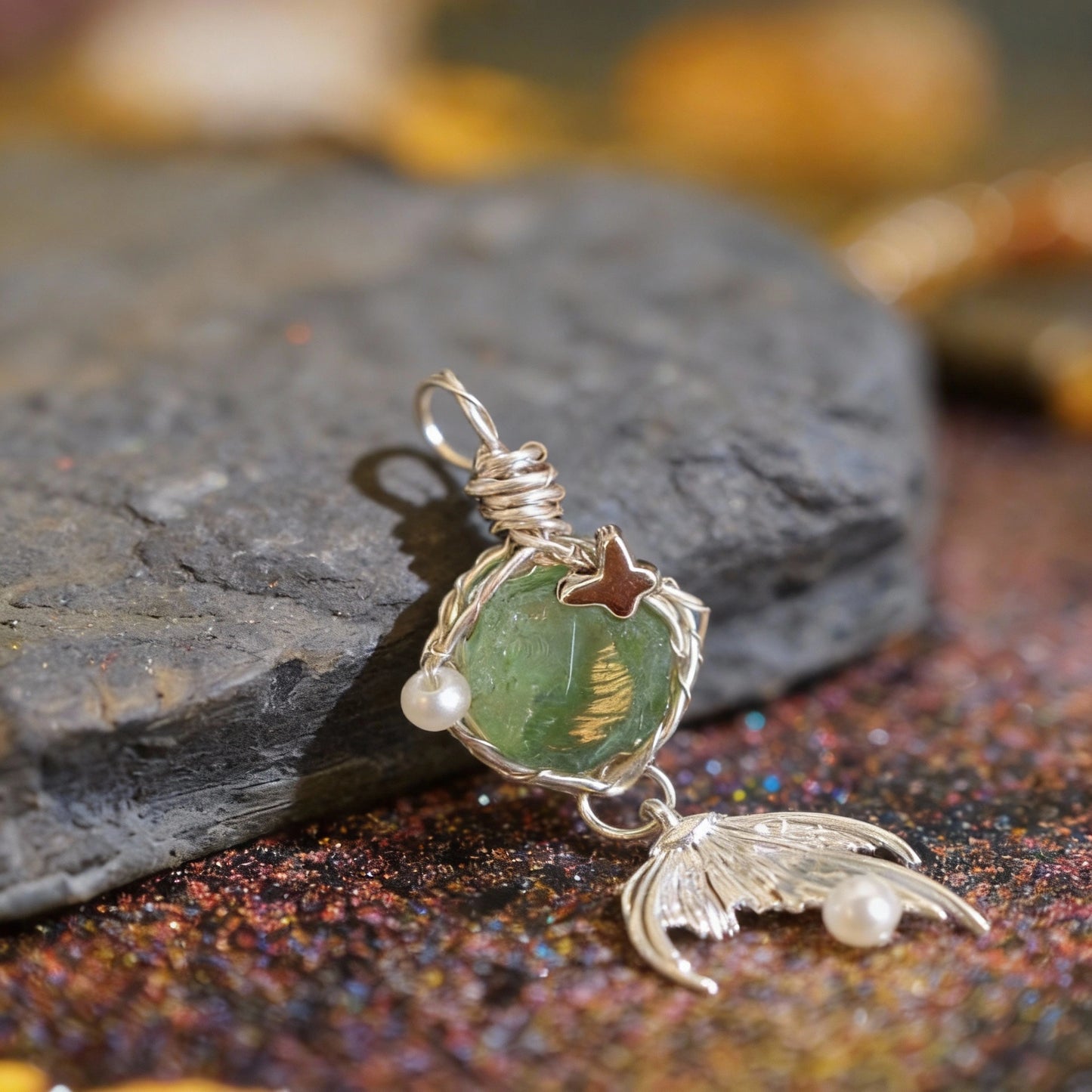 Pendant lying on a textured surface with warm bokeh lights, small dangle visible.