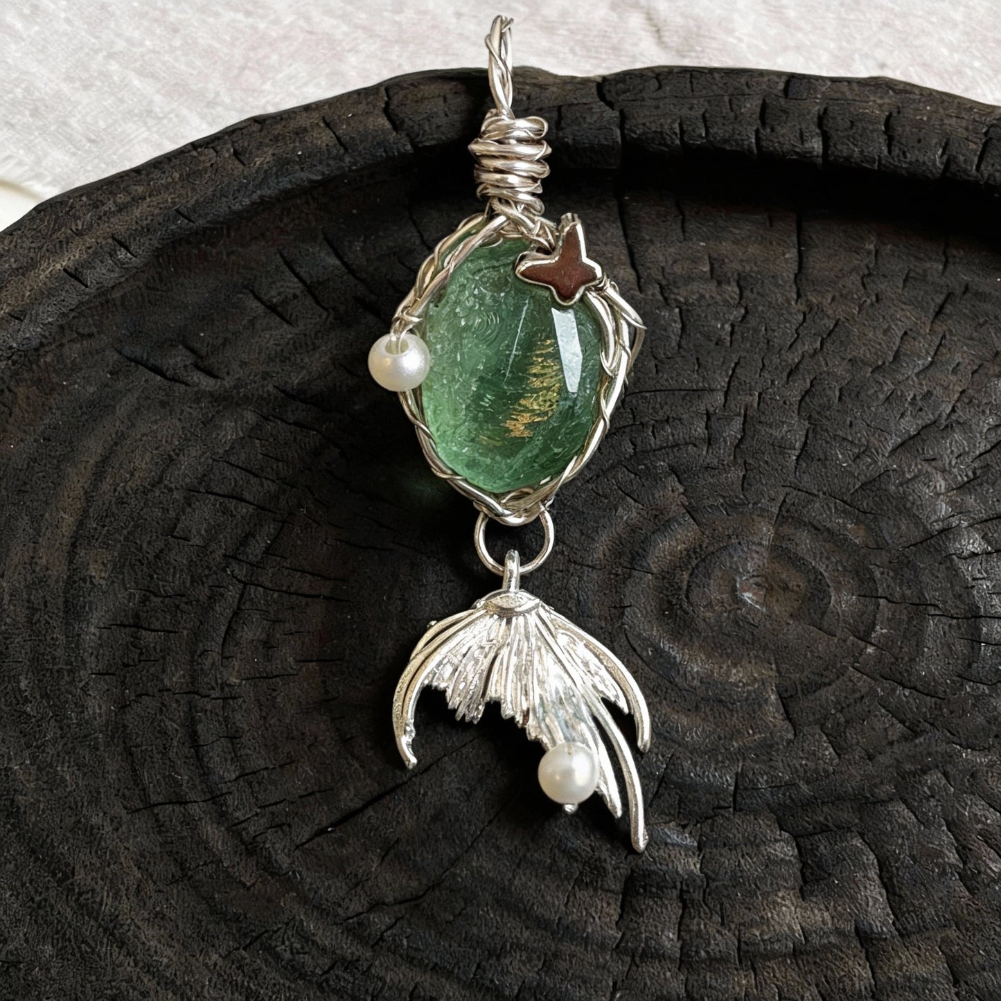 Pendant placed upright on a dark wooden plate, front view.