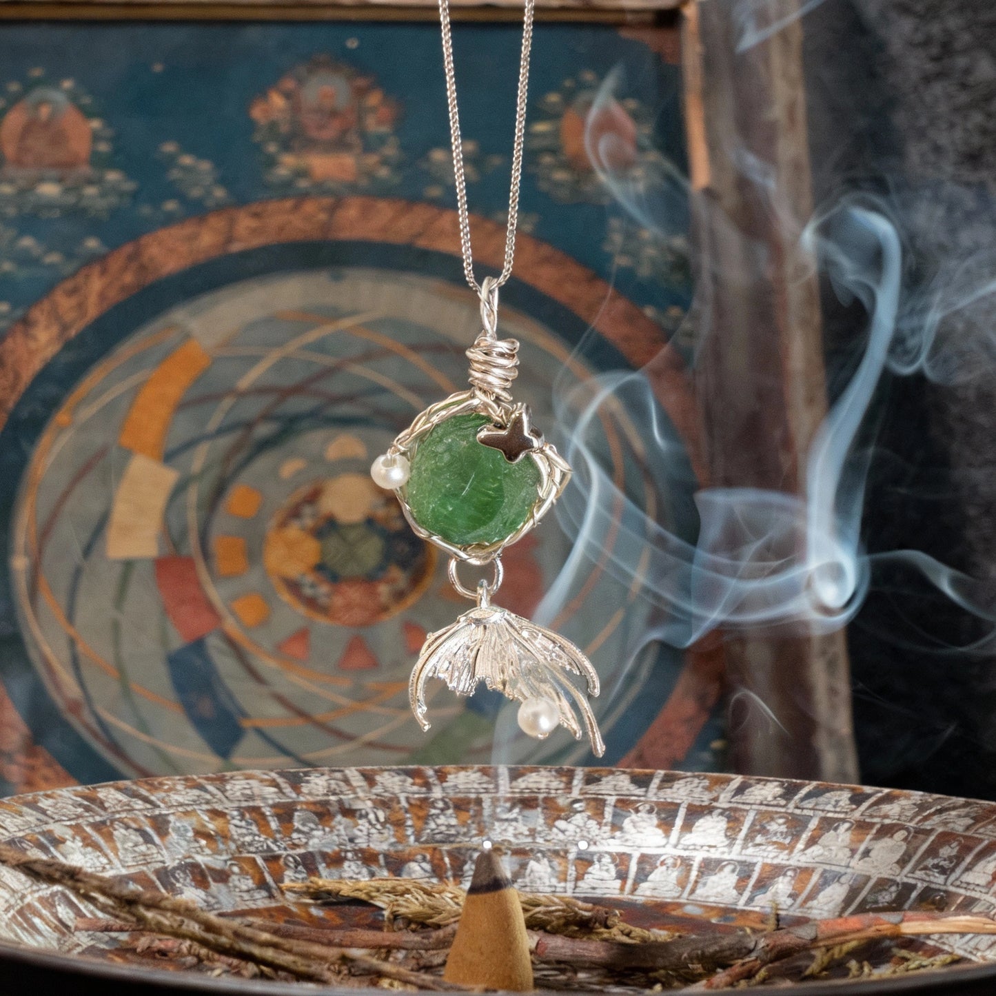 Pendant suspended above an incense burner with decorative backdrop and curling smoke.