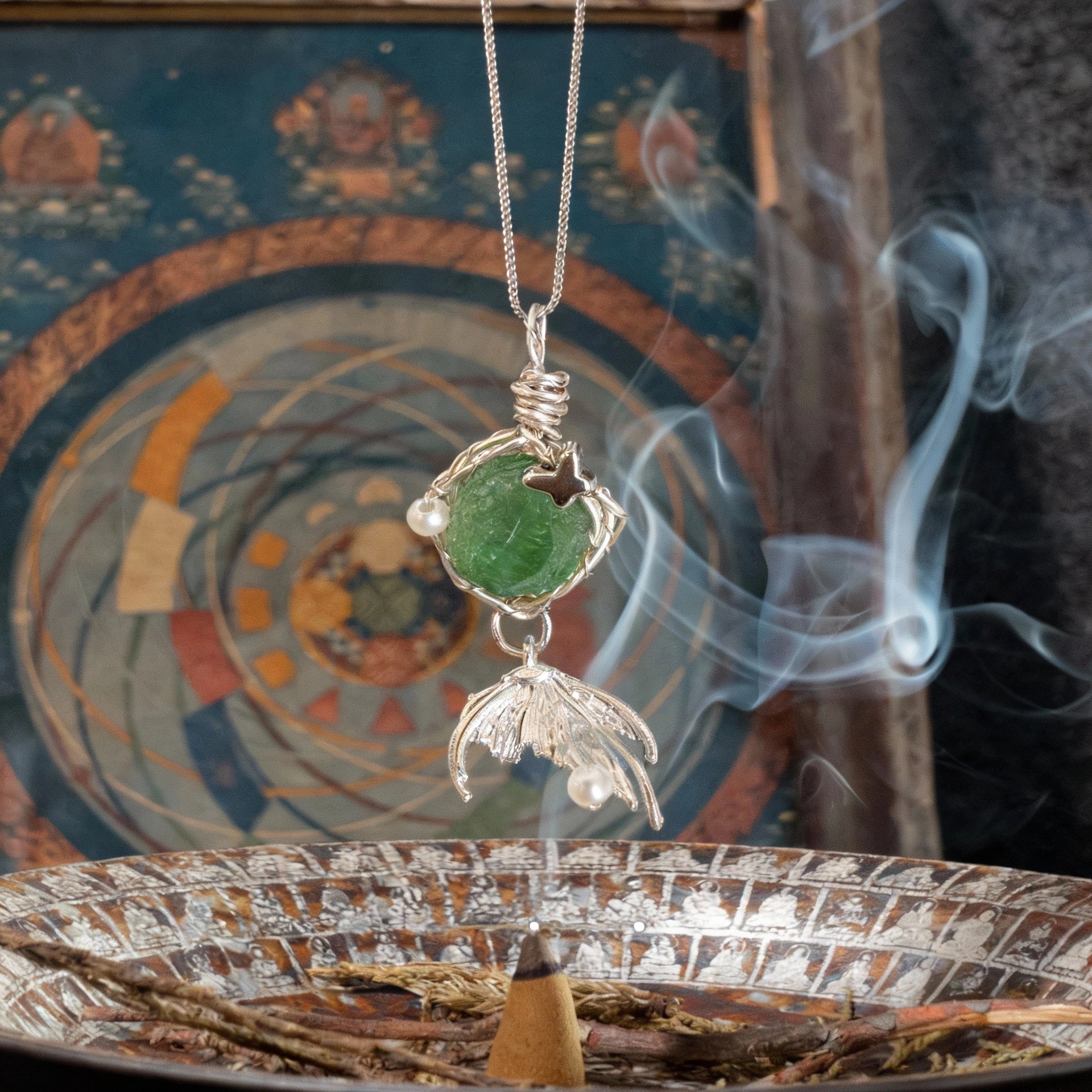 Pendant suspended above an incense burner with decorative backdrop and curling smoke.