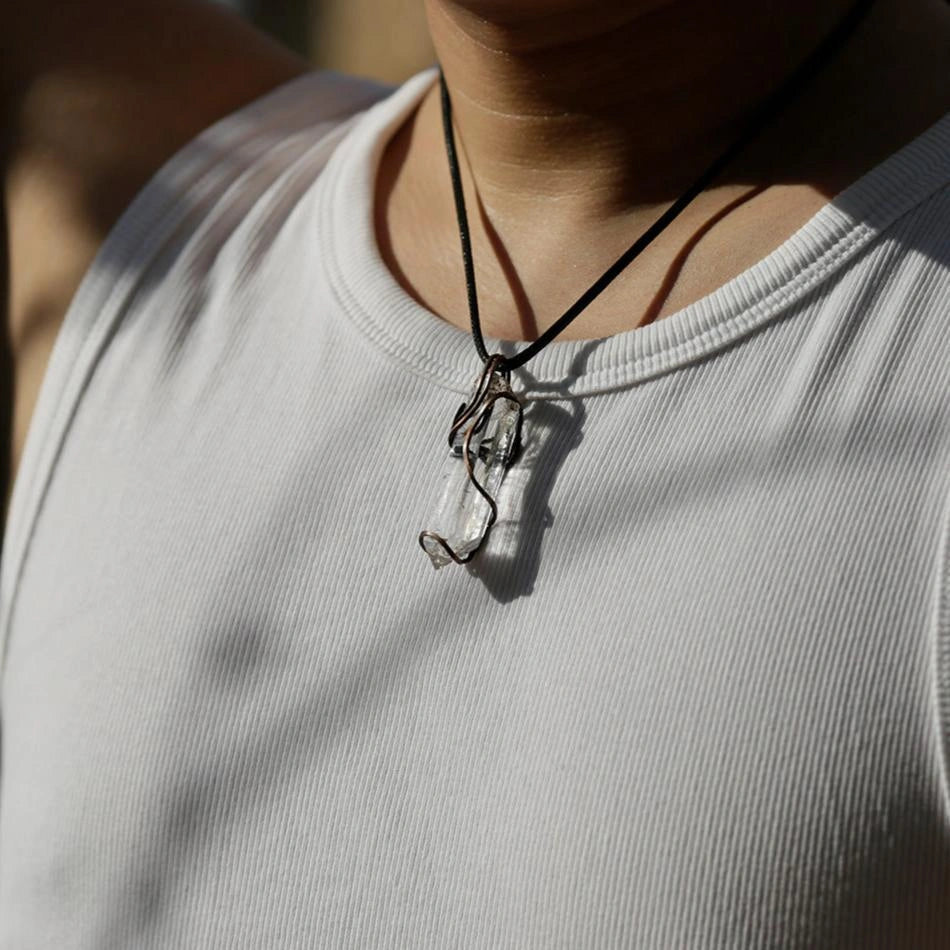 Pendant worn on a dark cord over a light T‑shirt, chest-level view.