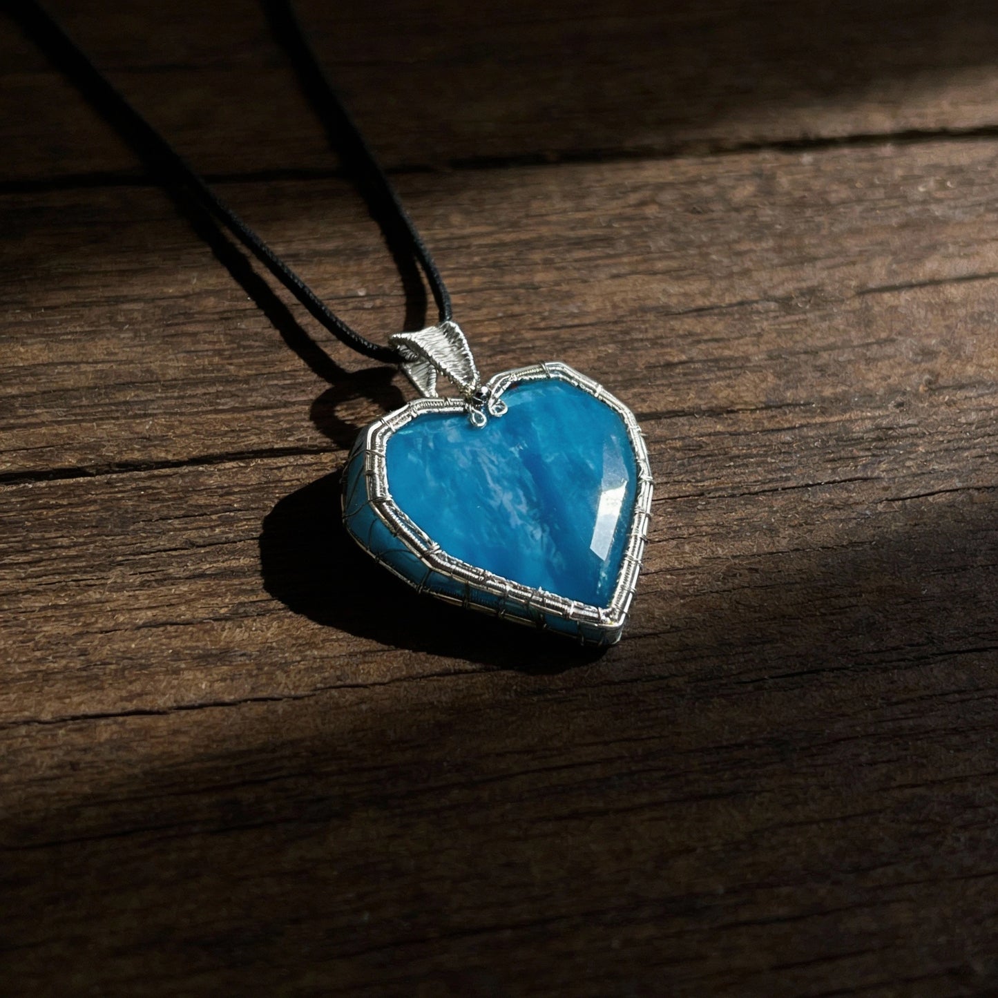 Pendant lying on a dark wooden tabletop, soft spotlight.