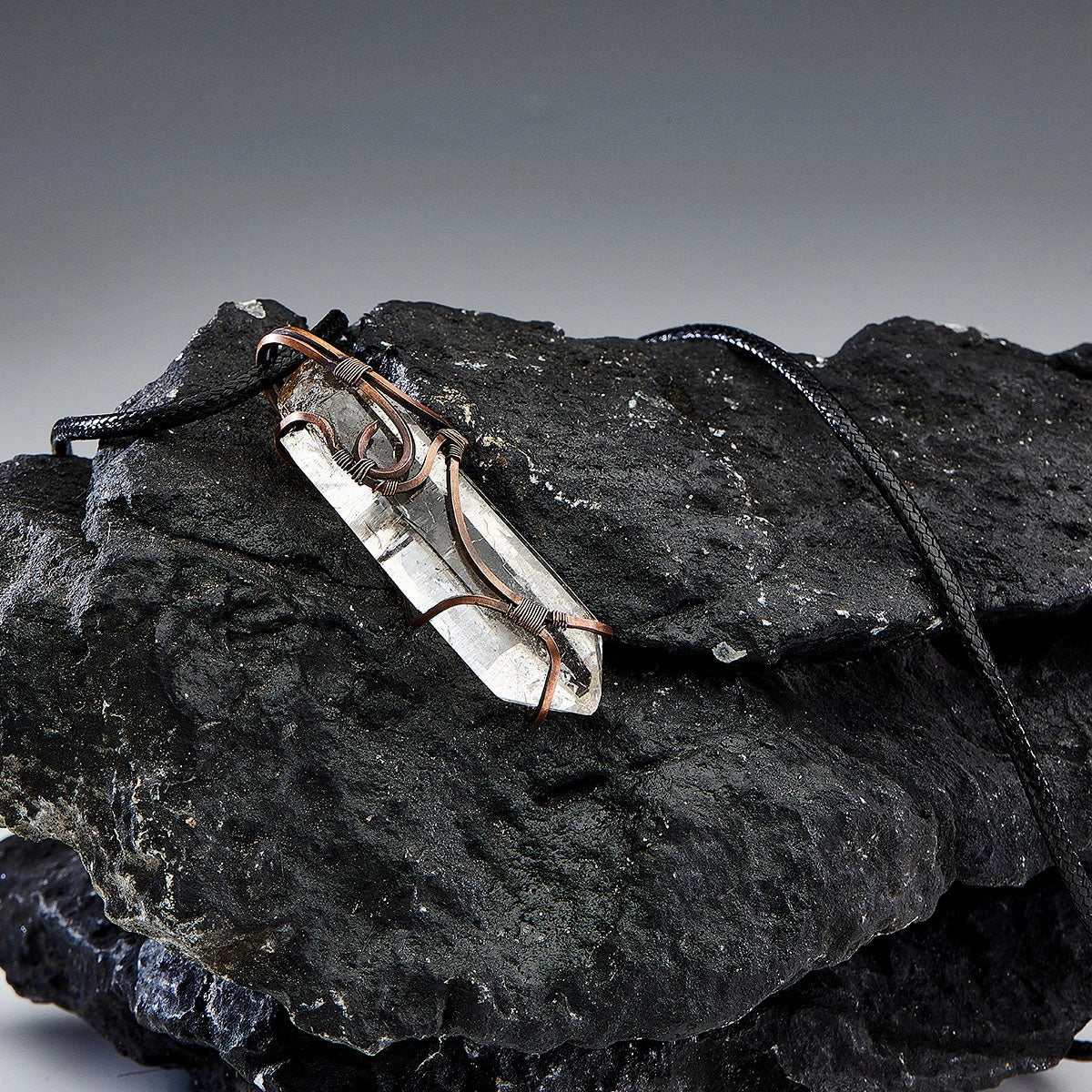 Pendant resting on stacked black rocks in studio lighting.