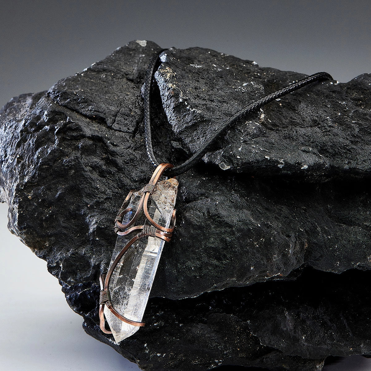 Another pendant on cord placed on black rocks, dark gray background.