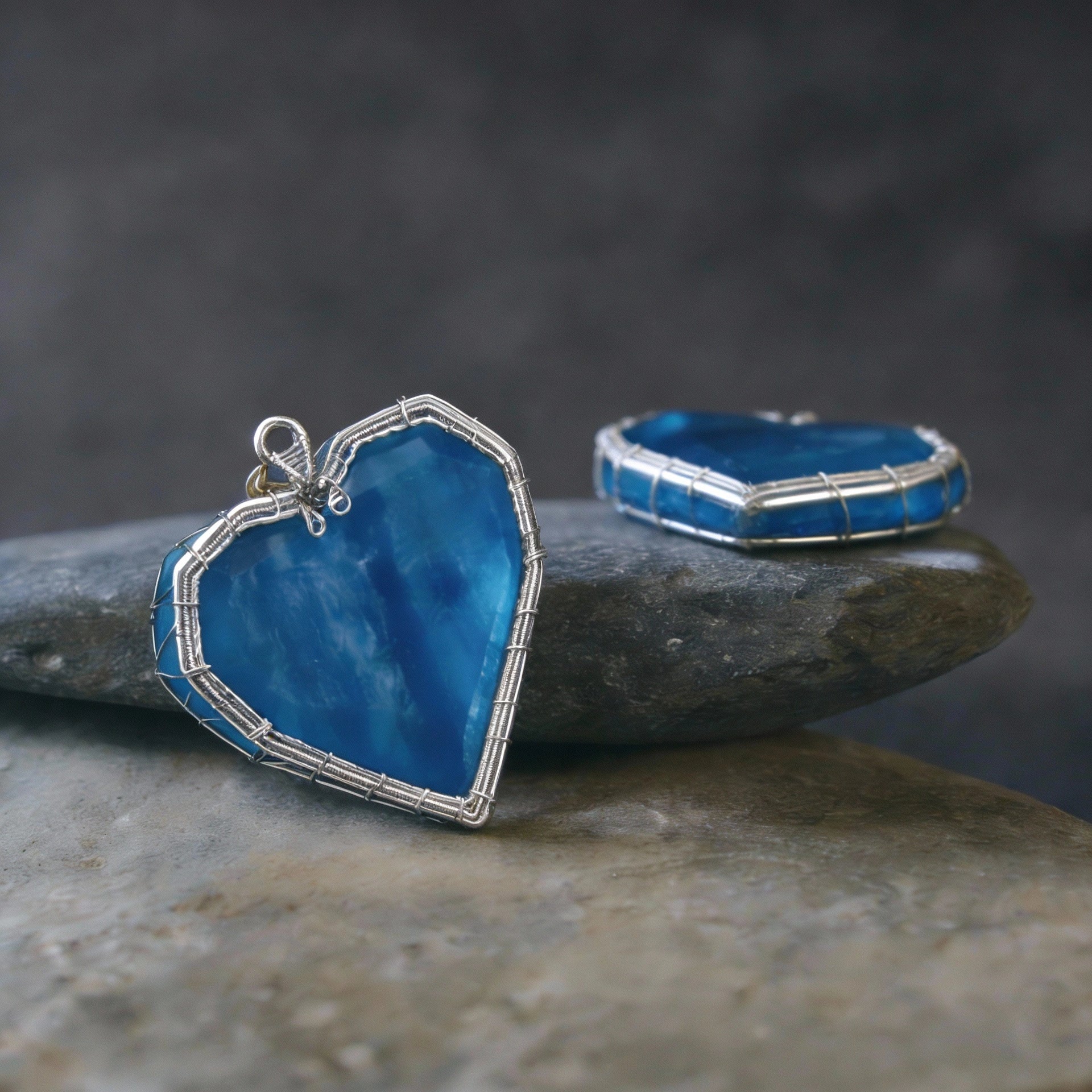 Pendant displayed on stacked smooth stones with a matching blue charm beside it.