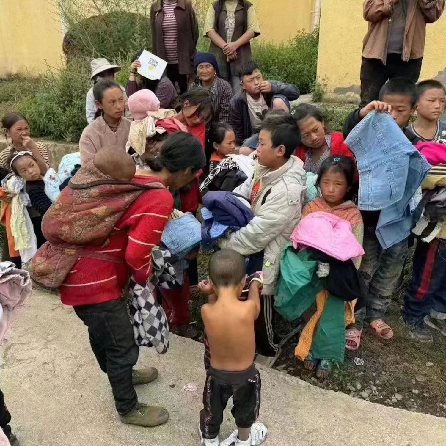 Community donation scene—villagers and children receive clothing in a rural courtyard, part of our Himalayan culture outreach that inspires mindful gifts like handmade crystal pendant, wire‑wrapped necklace, and boho spiritual jewelry supporting charity.