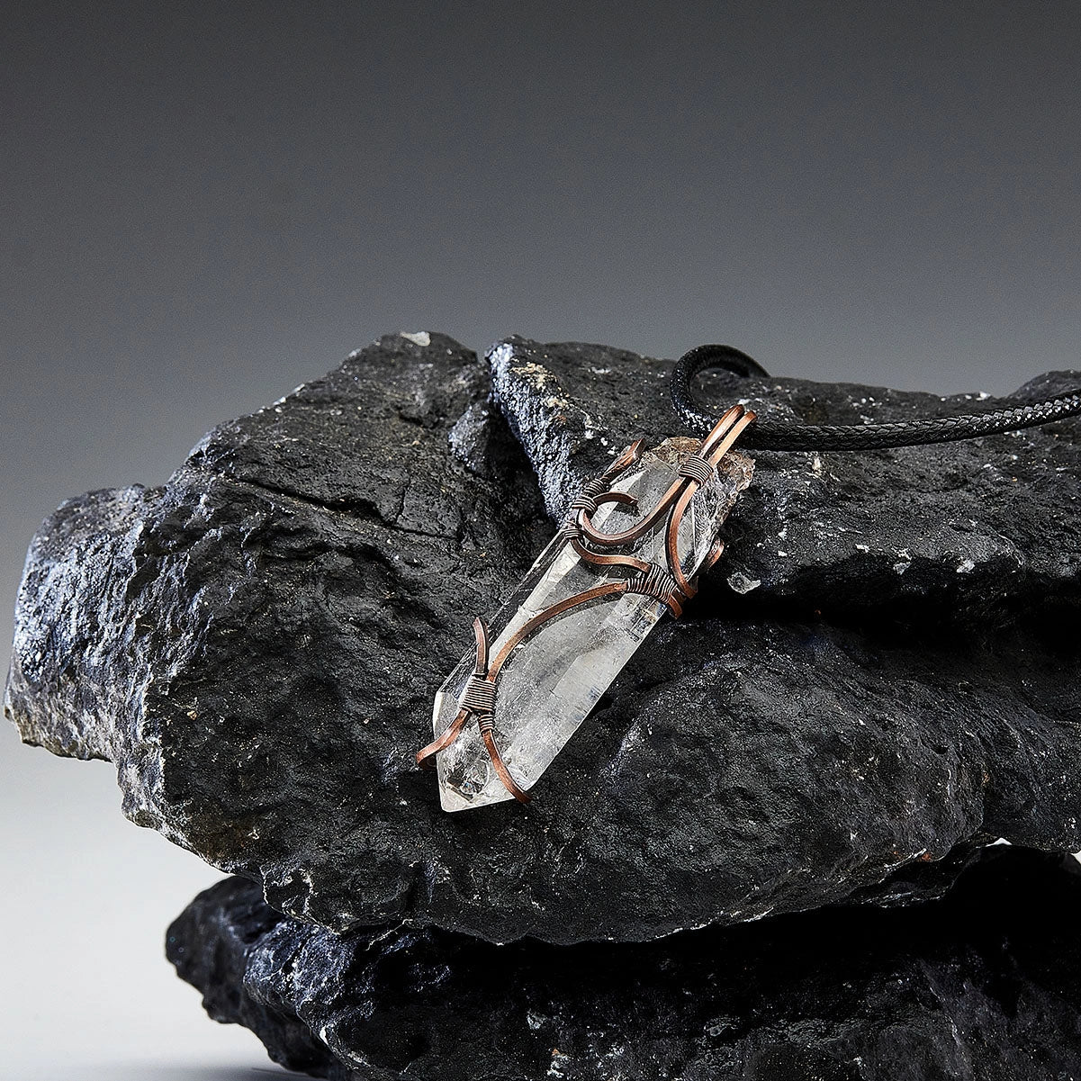 Close-up of pendant laid on black rocks, cord looped beside it.