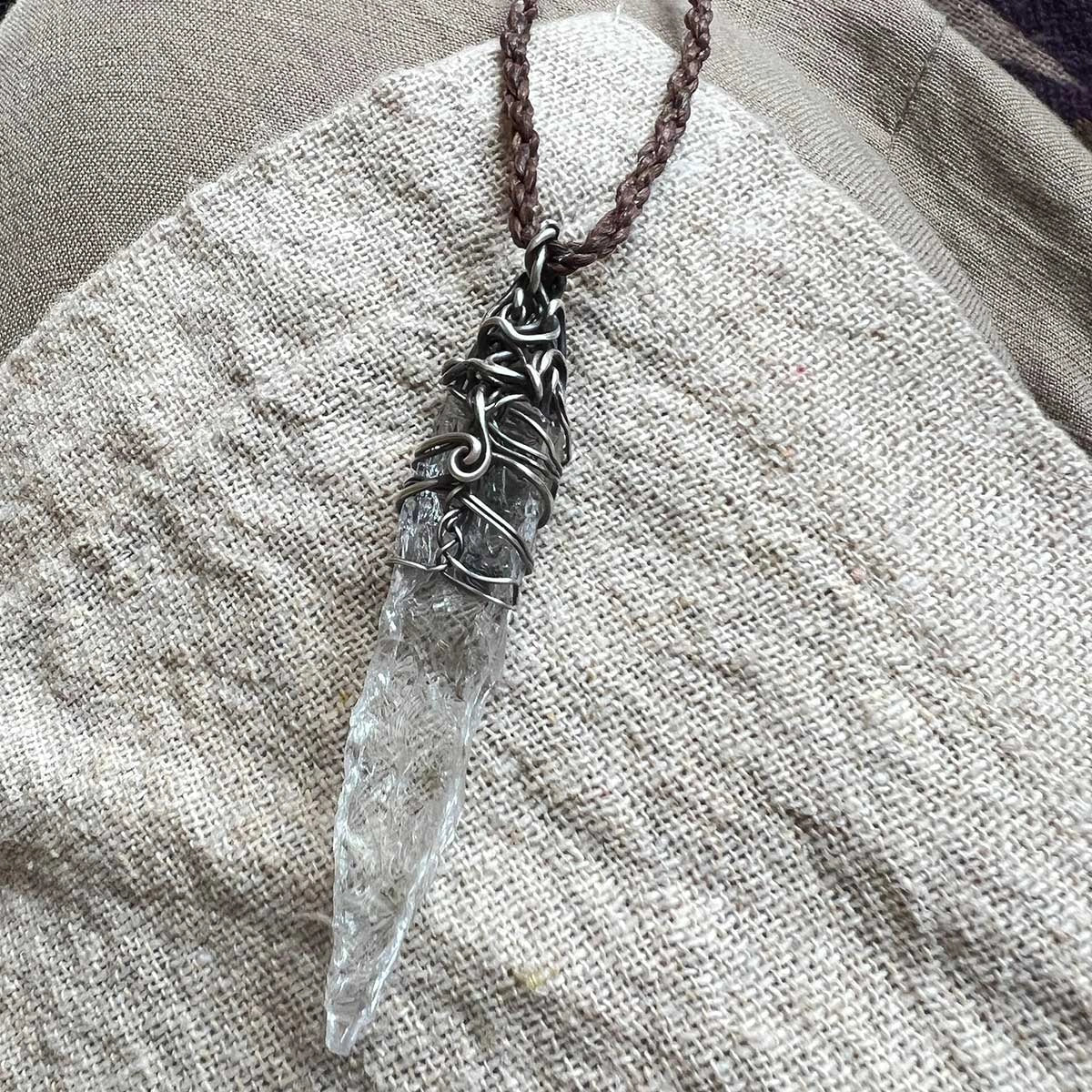 Pendant resting on a folded beige garment, cord visible.