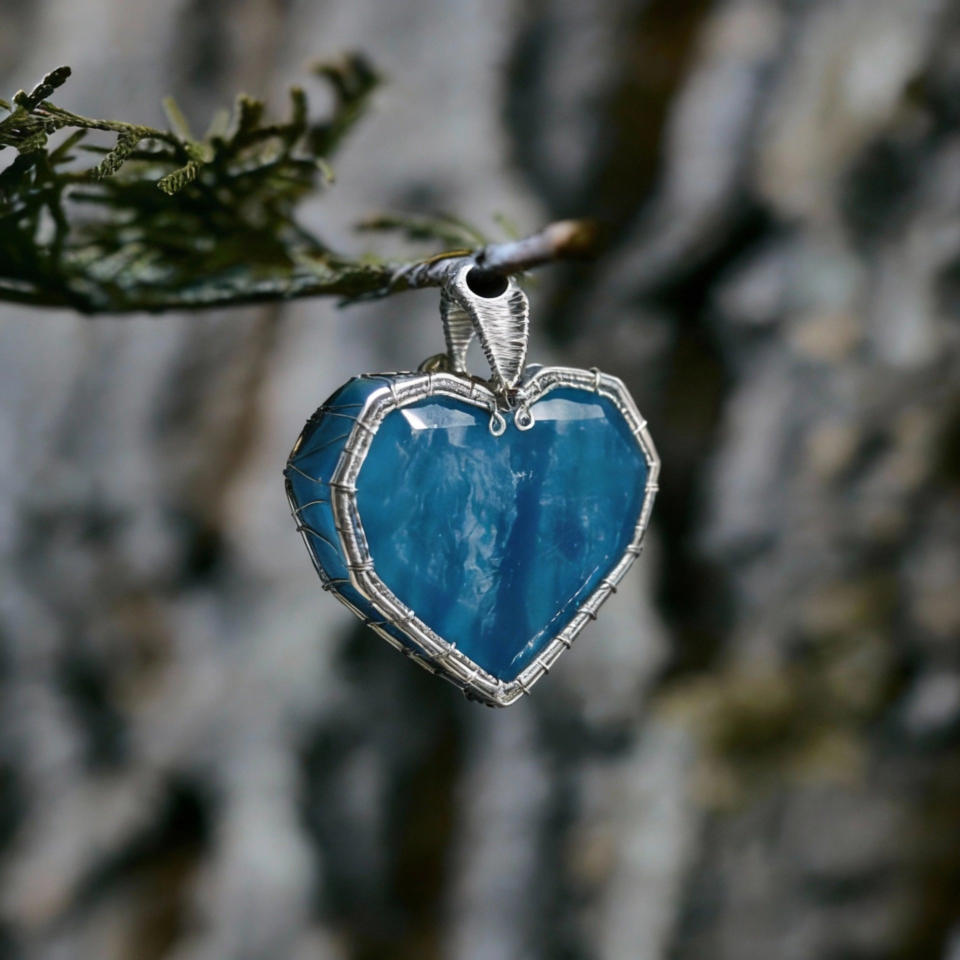 Pendant hanging from a small branch against tree-bark background.