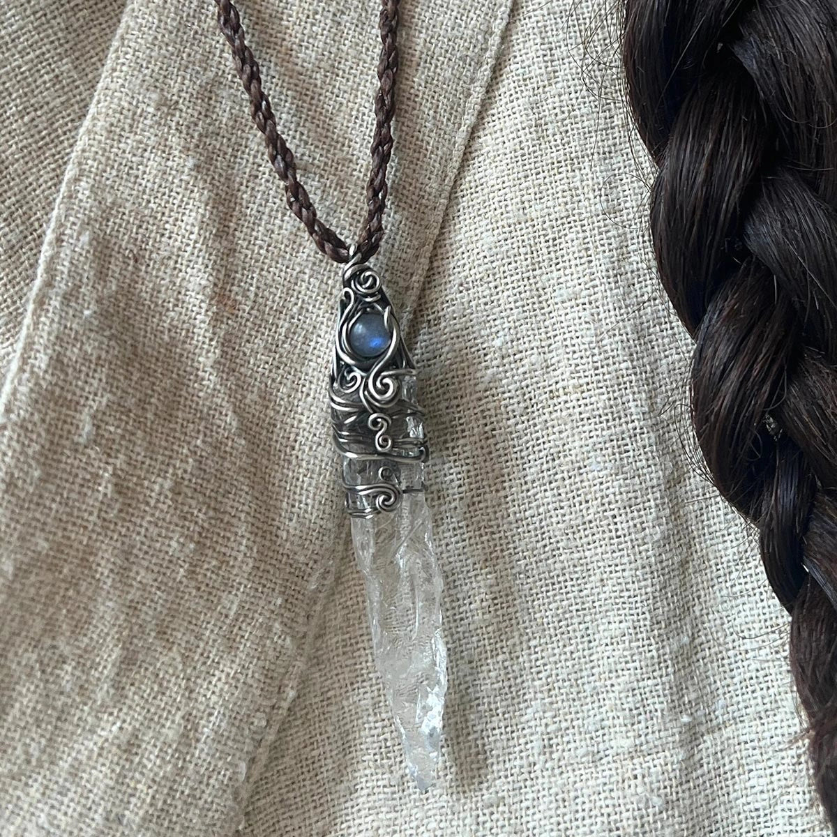 Pendant worn on a beige top beside a dark braid.