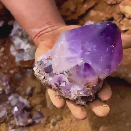 Hand holding a rough amethyst chunk outdoors.