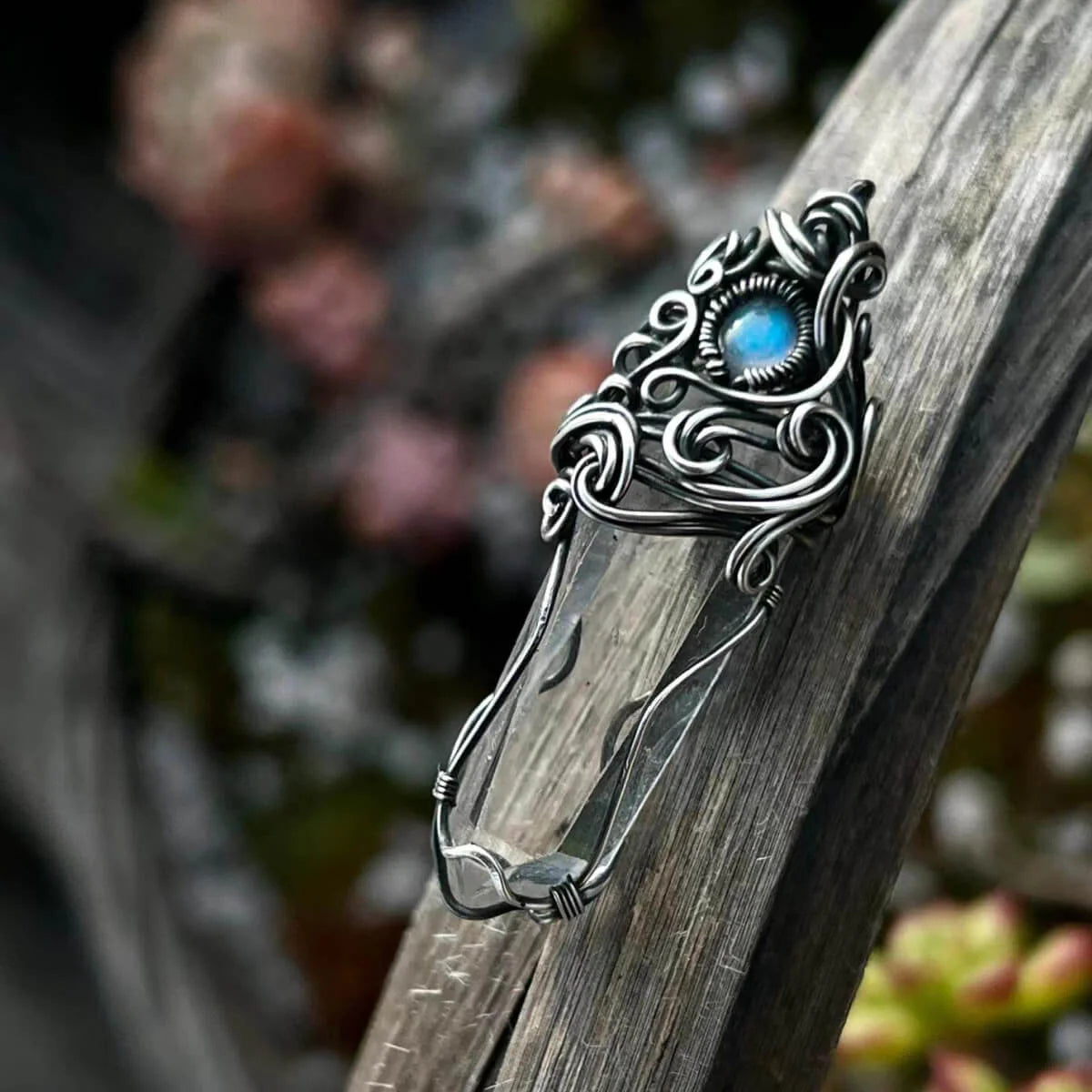Close-up of the same pendant with a blue stone resting on a tree branch.