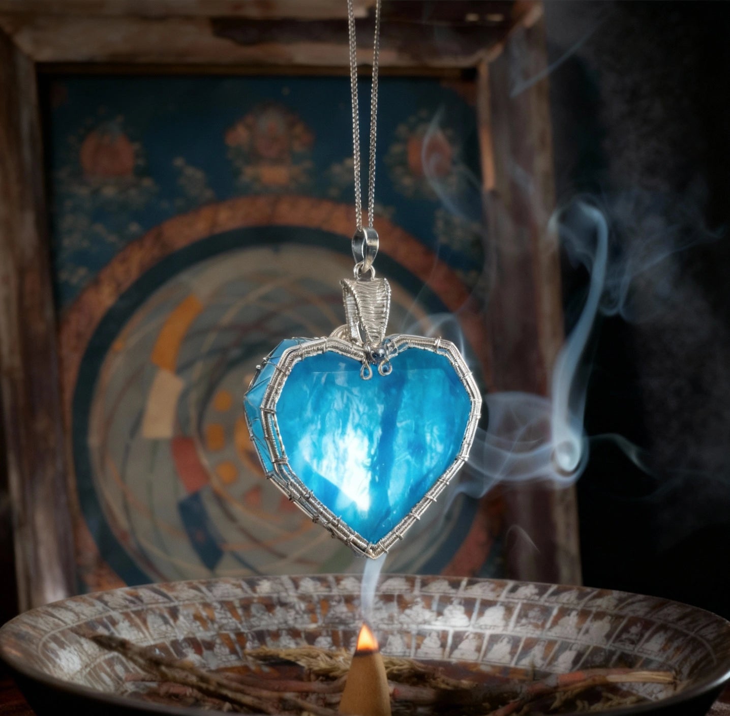 Pendant suspended above an incense burner with decorative backdrop and curling smoke.