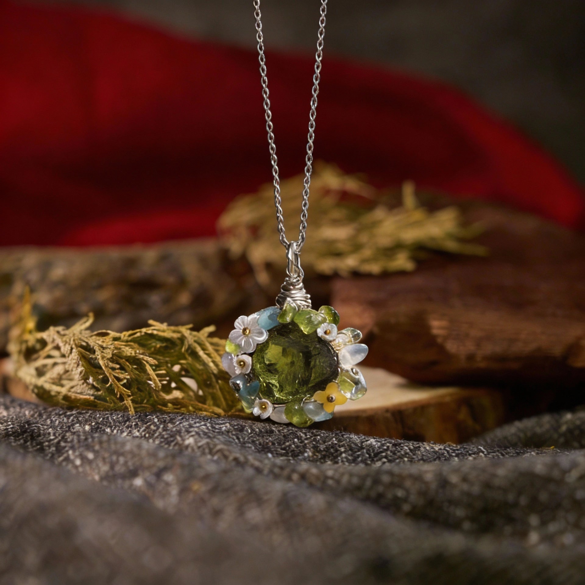 Pendant lying on fabric with dried plants and a red cloth in the background.