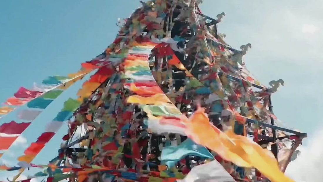 Tibetan prayer flags flutter; a woman ties blue flags and prays at sunset by a lake—evoking mindful ritual for handmade crystal pendant, wire‑wrapped necklace, boho spiritual jewelry.